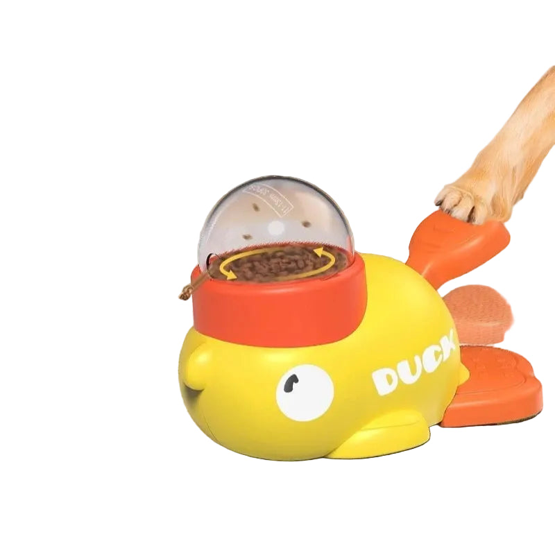 Yellow duck-shaped toy with a red top, pressable to release treats, on a carpeted floor.