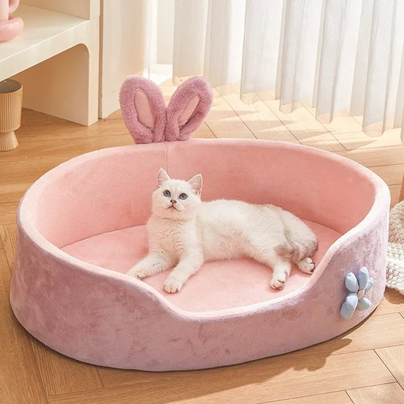 Pink pet bed with bunny ears and a white cat inside, on a wooden floor.

